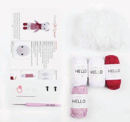 Pink and white yarn skeins with crochet pattern, needle, and cute bunny project instructions