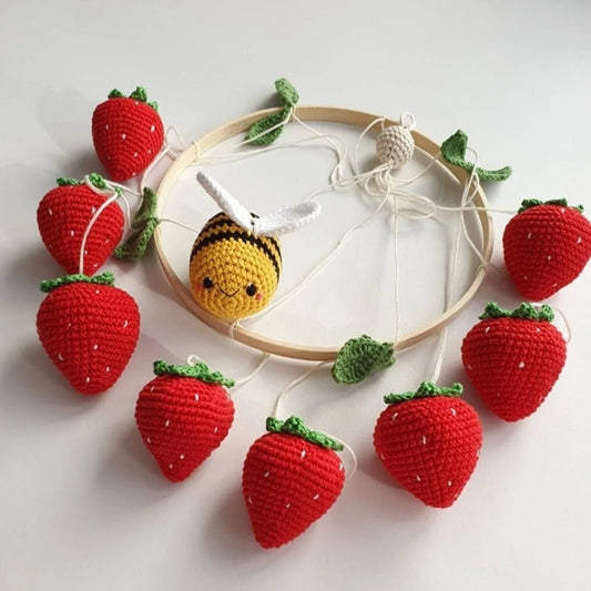 Crocheted red strawberries and a yellow bee around an embroidery hoop with strings