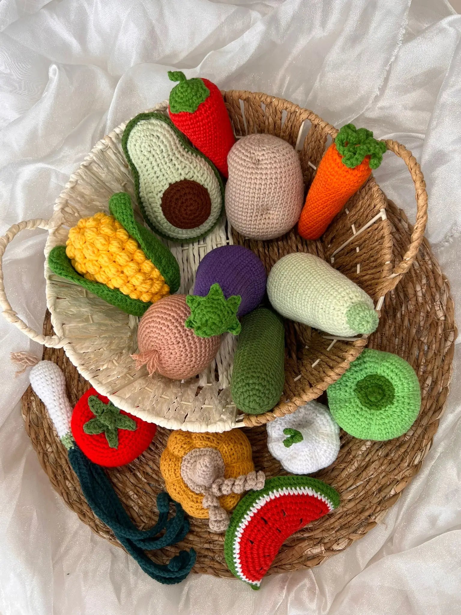 Crocheted fruits and vegetables in a woven basket on white fabric background