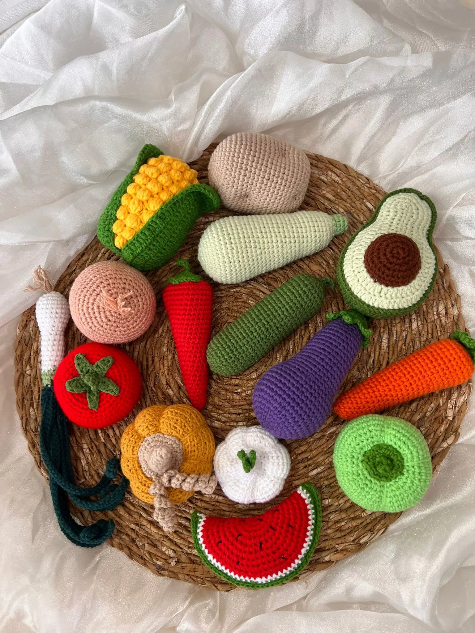 Crocheted fruits and vegetables on a woven basket, arranged on white fabric background