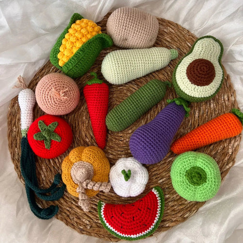 Crocheted fruits and vegetables on a woven basket, arranged on white fabric background