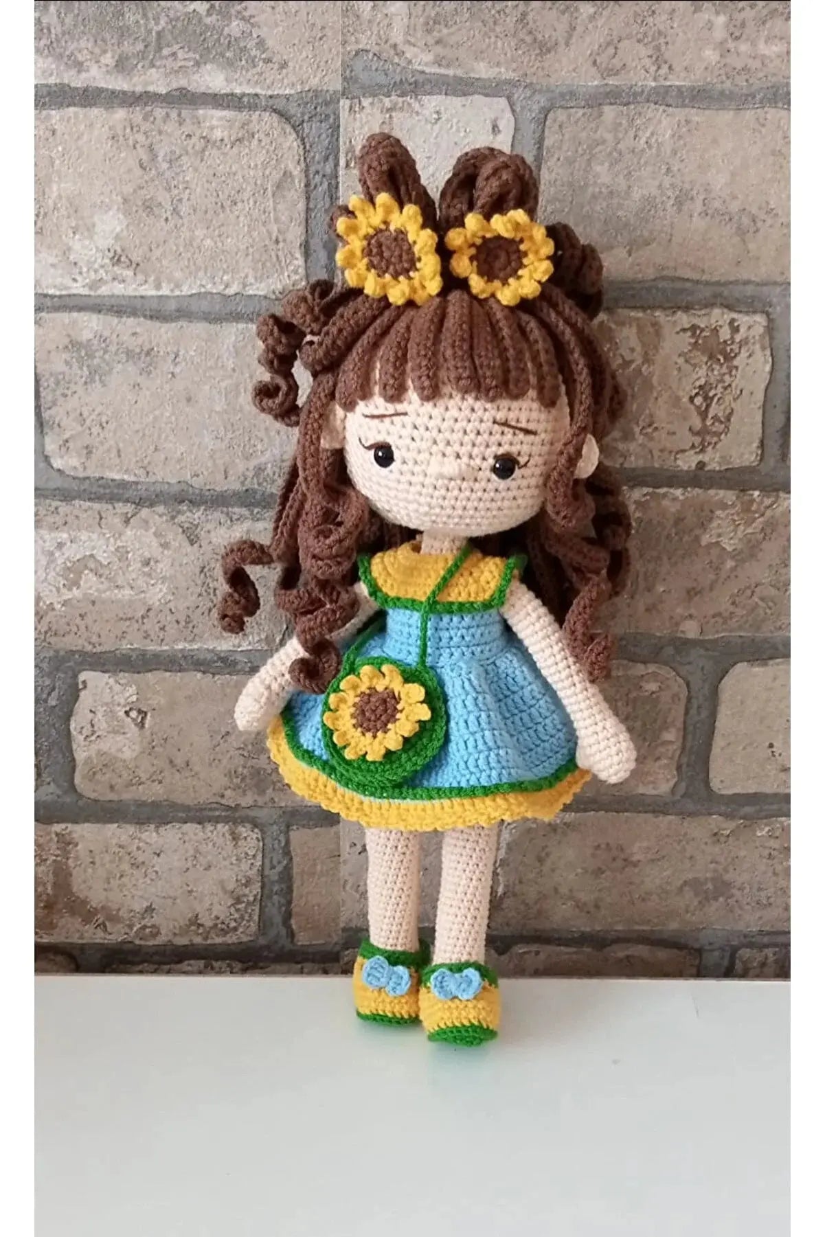 a crocheted doll is standing next to a brick wall