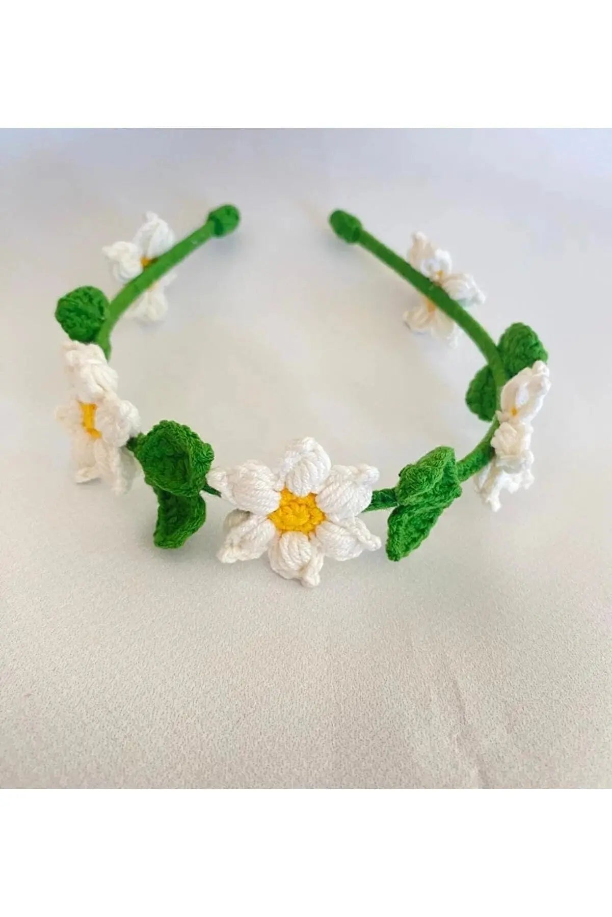 a crocheted headband with white flowers and green leaves