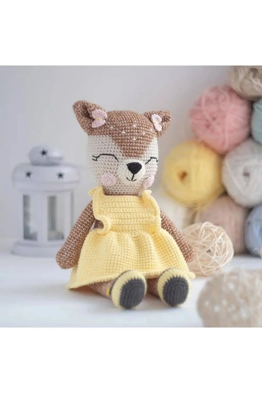 a teddy bear wearing a yellow dress sitting next to a pile of balls of yarn