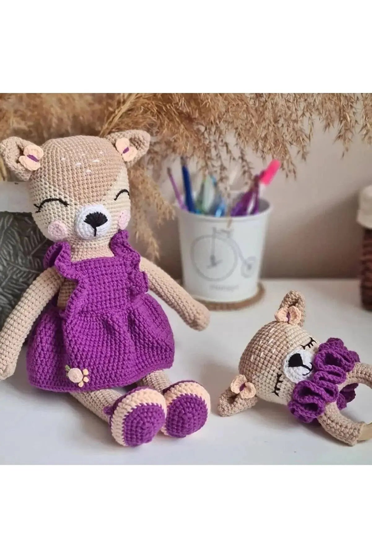 a crocheted teddy bear in a purple dress next to a smaller teddy bear