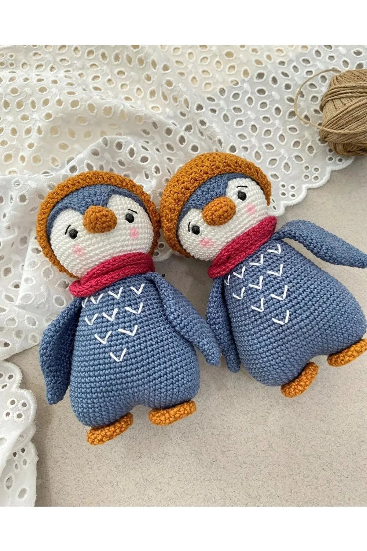 two crocheted penguin dolls sitting next to a ball of yarn