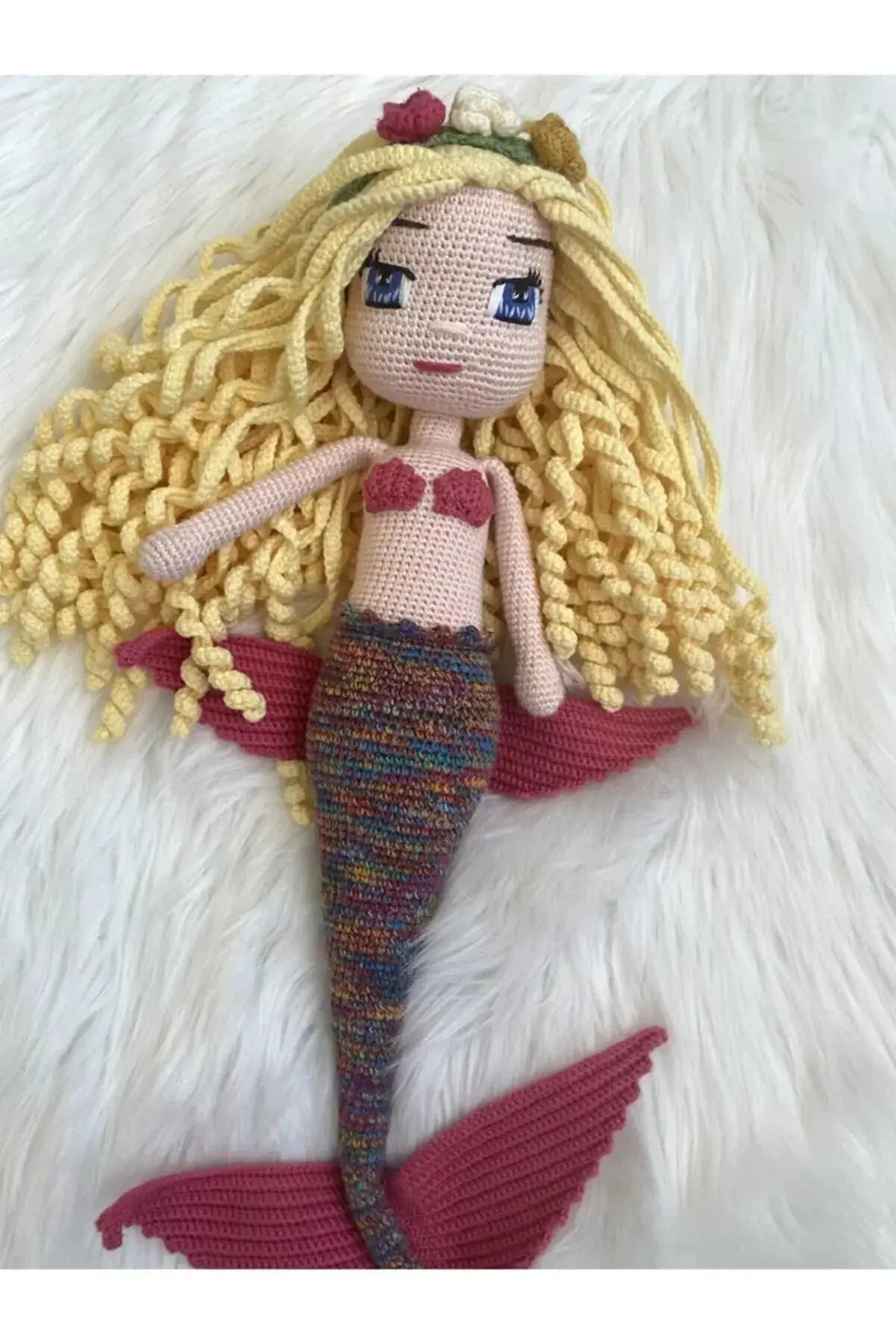 a knitted mermaid doll laying on top of a white blanket