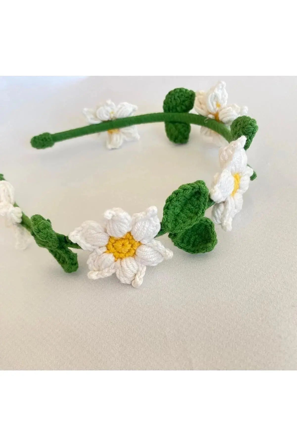 a crocheted headband with white flowers and green leaves