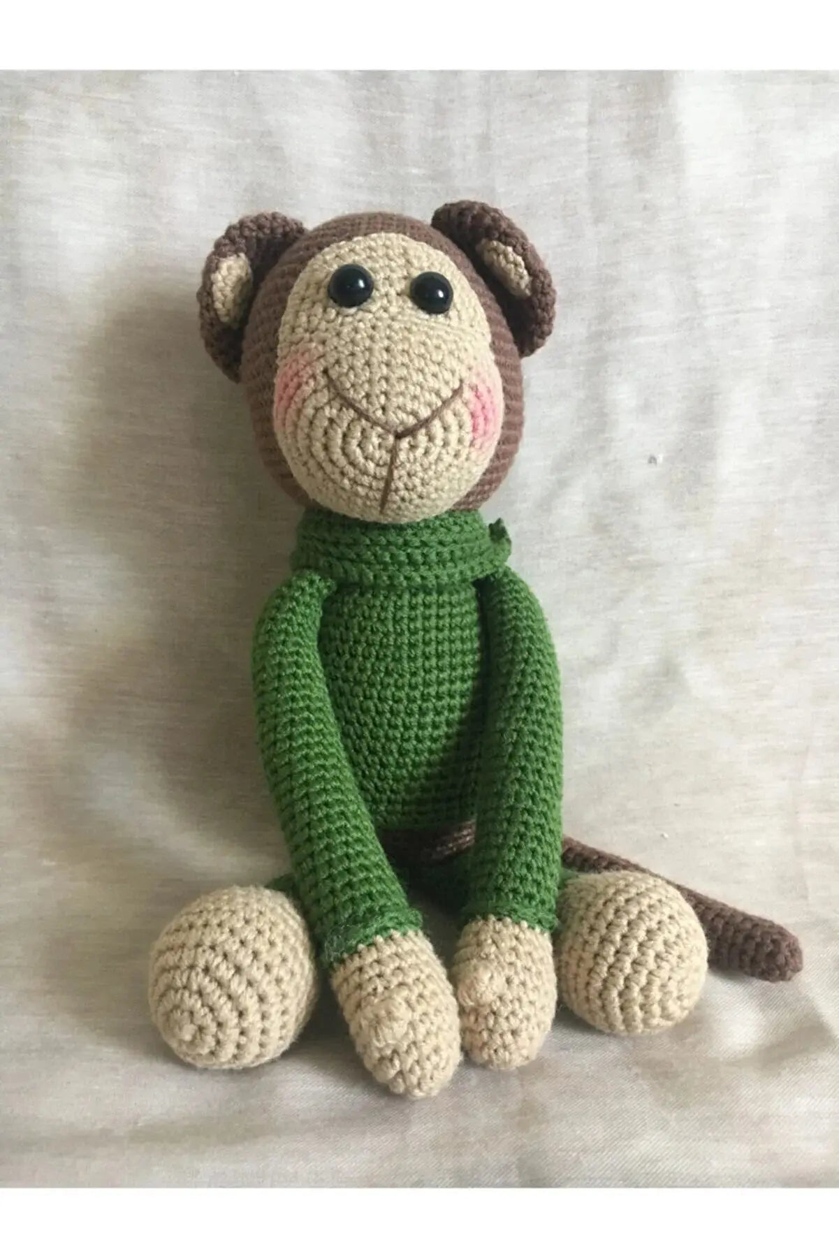 a crocheted monkey sitting on a white sheet