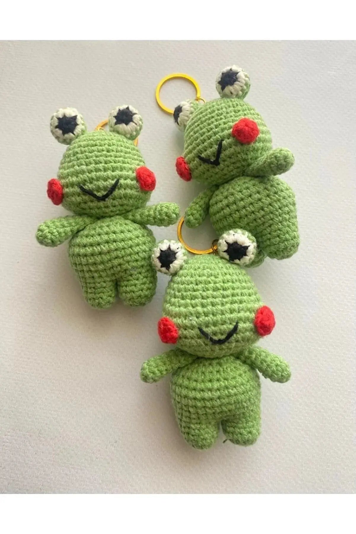 three crocheted frog keychains on a white surface