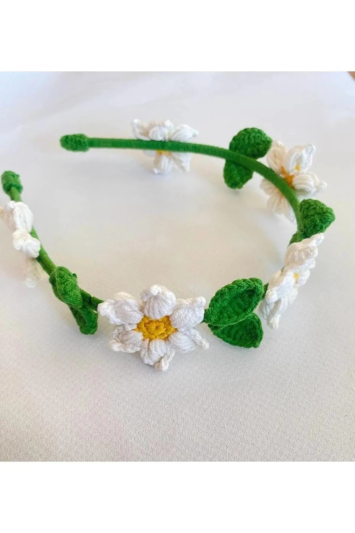 a crocheted headband with white flowers and green leaves