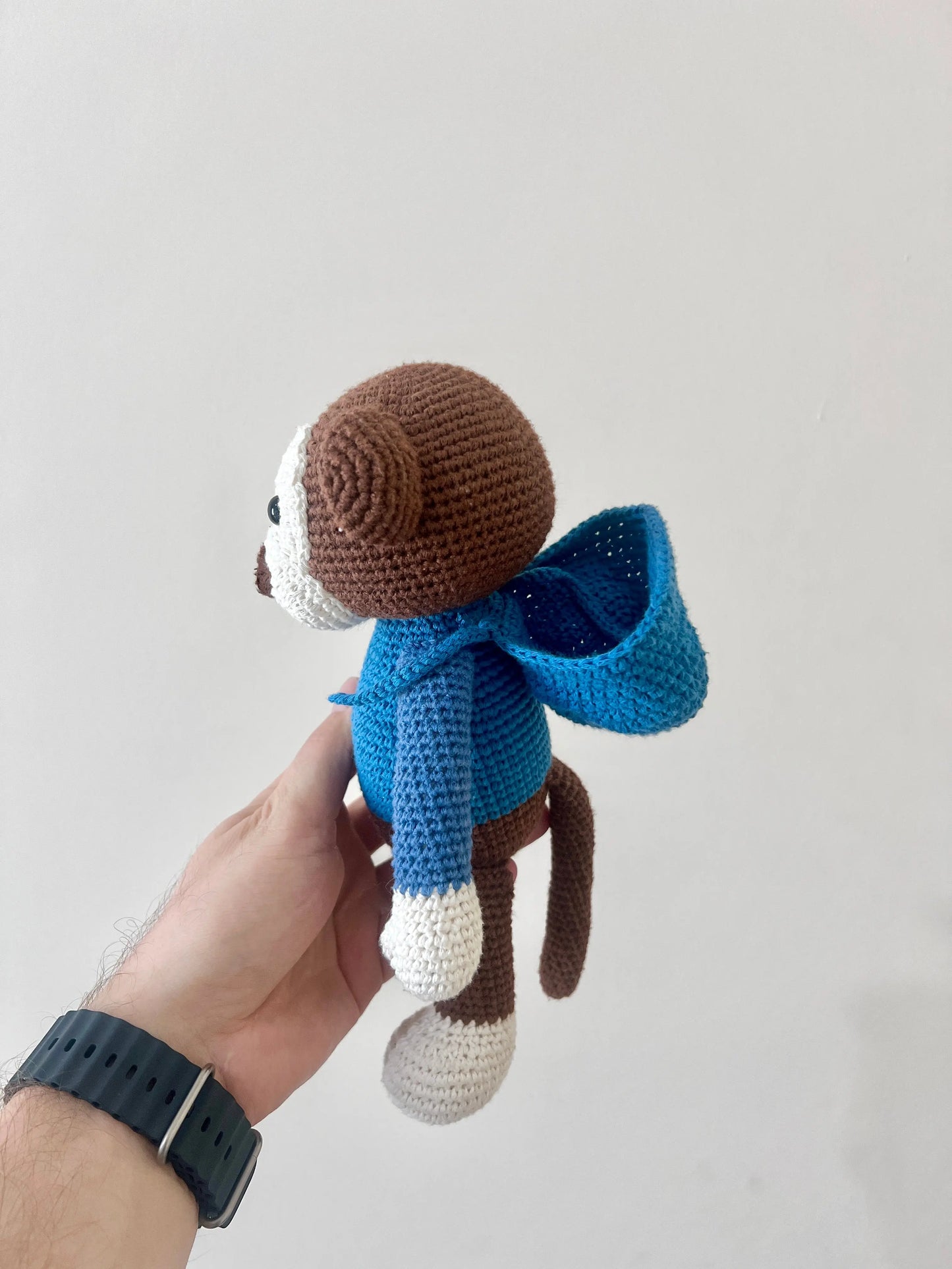 a hand holding a small crocheted monkey