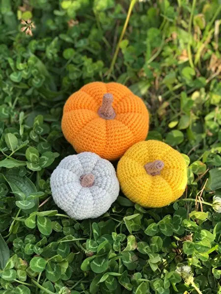 three crocheted pumpkins sitting in the grass