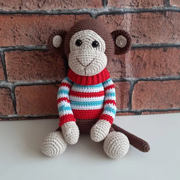 a crocheted monkey sitting against a brick wall