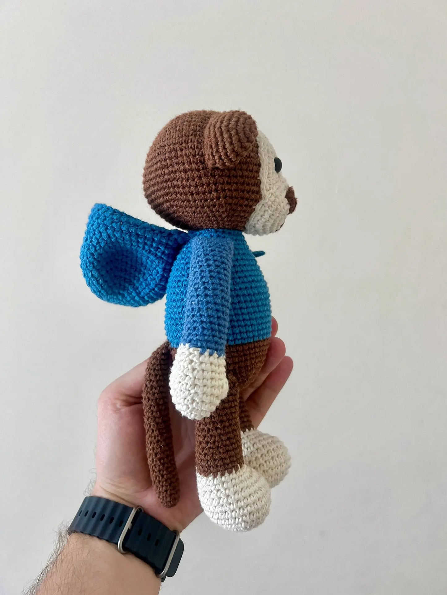 a hand holding a small crocheted teddy bear