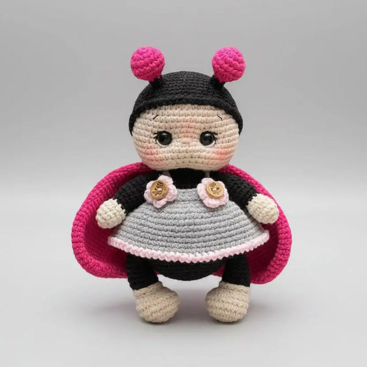 Crocheted ladybug doll with pink antennae and cute gray dress on gray background