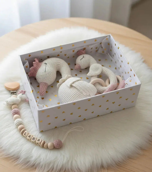 Crocheted baby toys in heart-patterned box with personalized pacifier clip on fur rug