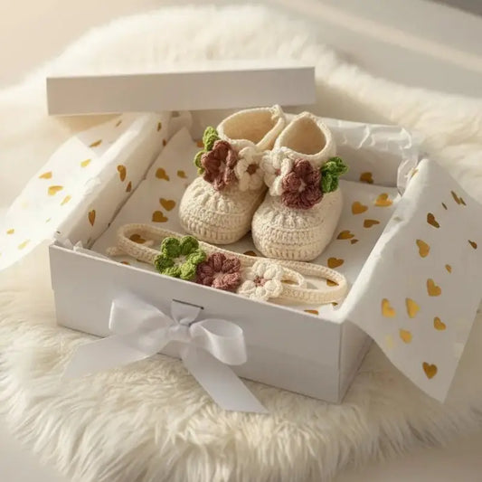 Handmade cream crochet baby booties with floral details in a white gift box with hearts