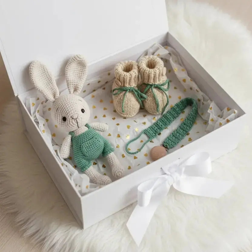 Knitted baby bunny, booties, and paceholder in a white gift box with gold hearts