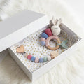 Handmade crochet baby toys in pastel colors, including bunny and teething ring, in gift box