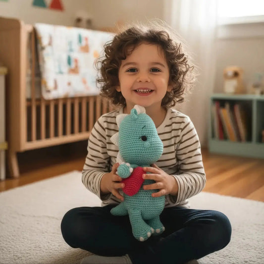 Child smiling and holding a teal crocheted dinosaur toy while sitting on a white rug