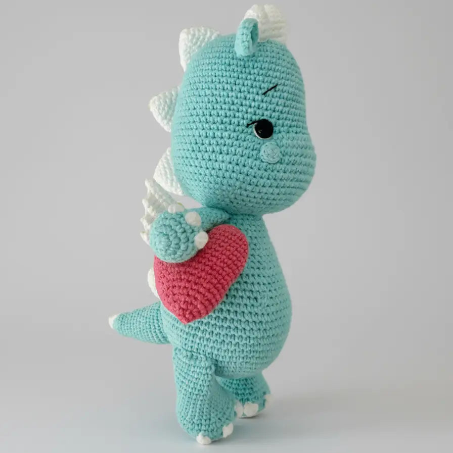 Teal crocheted dinosaur plush with white spikes and a red heart, side view