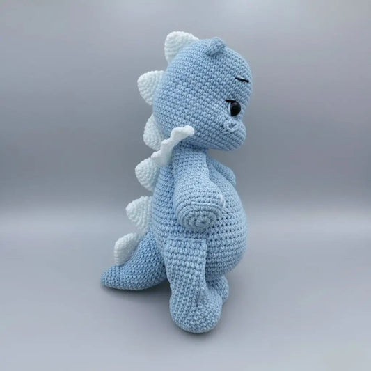 Blue crocheted dinosaur plush toy with white spiky back and cute button eye