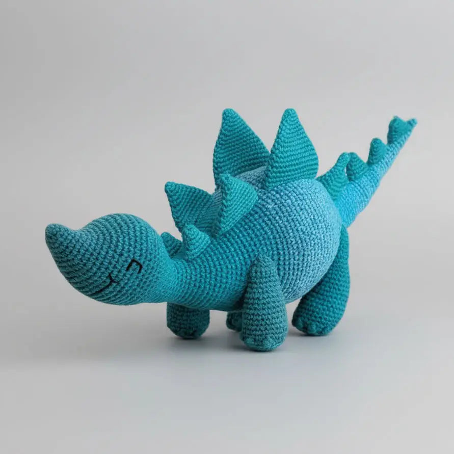Teal crocheted stegosaurus stuffed animal with textured yarn on neutral background