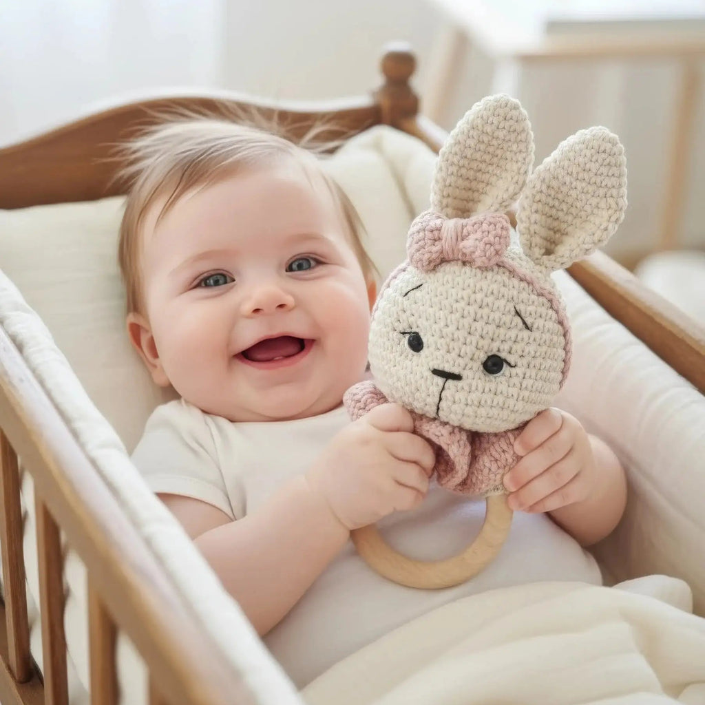 Smiling baby holding crocheted bunny toy in wooden crib with soft white bedding