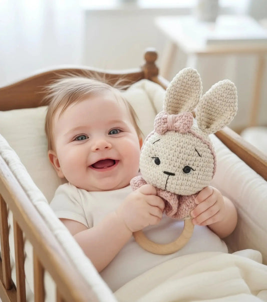Smiling baby holding crocheted bunny toy in wooden crib with soft white bedding