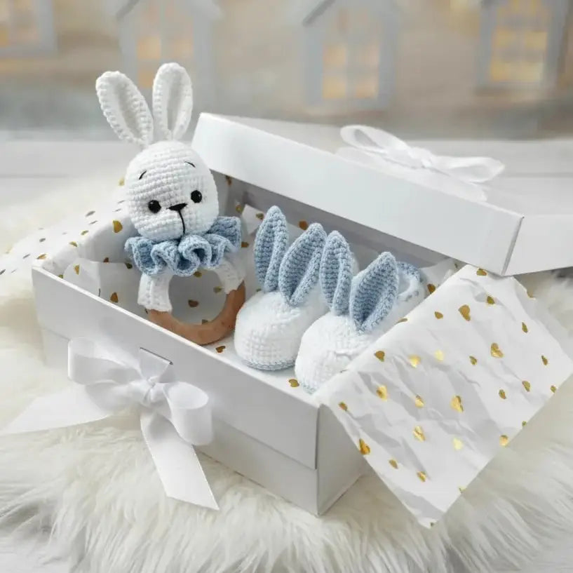 Crocheted white bunny and blue baby booties in a gift box with gold polka dots