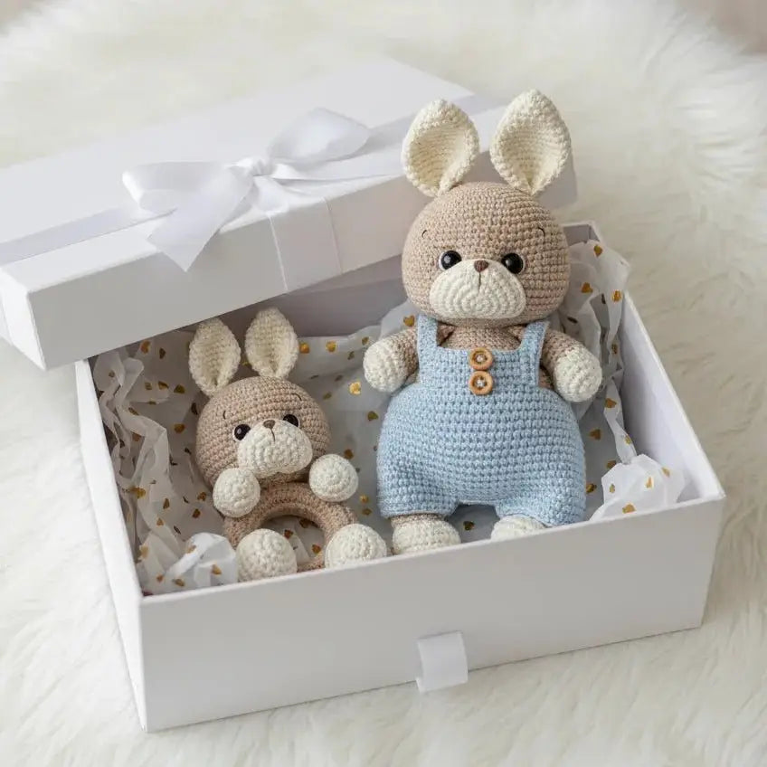 Two crocheted bunny dolls in a white gift box with gold-speckled tissue paper and a white ribbon.