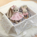 Crocheted bunny dolls in pink dress and teething ring, nestled in a gift box with gold hearts