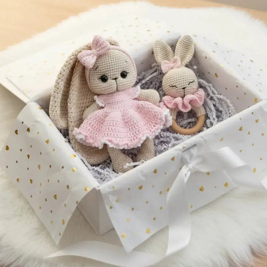 Crocheted bunny dolls in pink dress and teething ring, nestled in a gift box with gold hearts