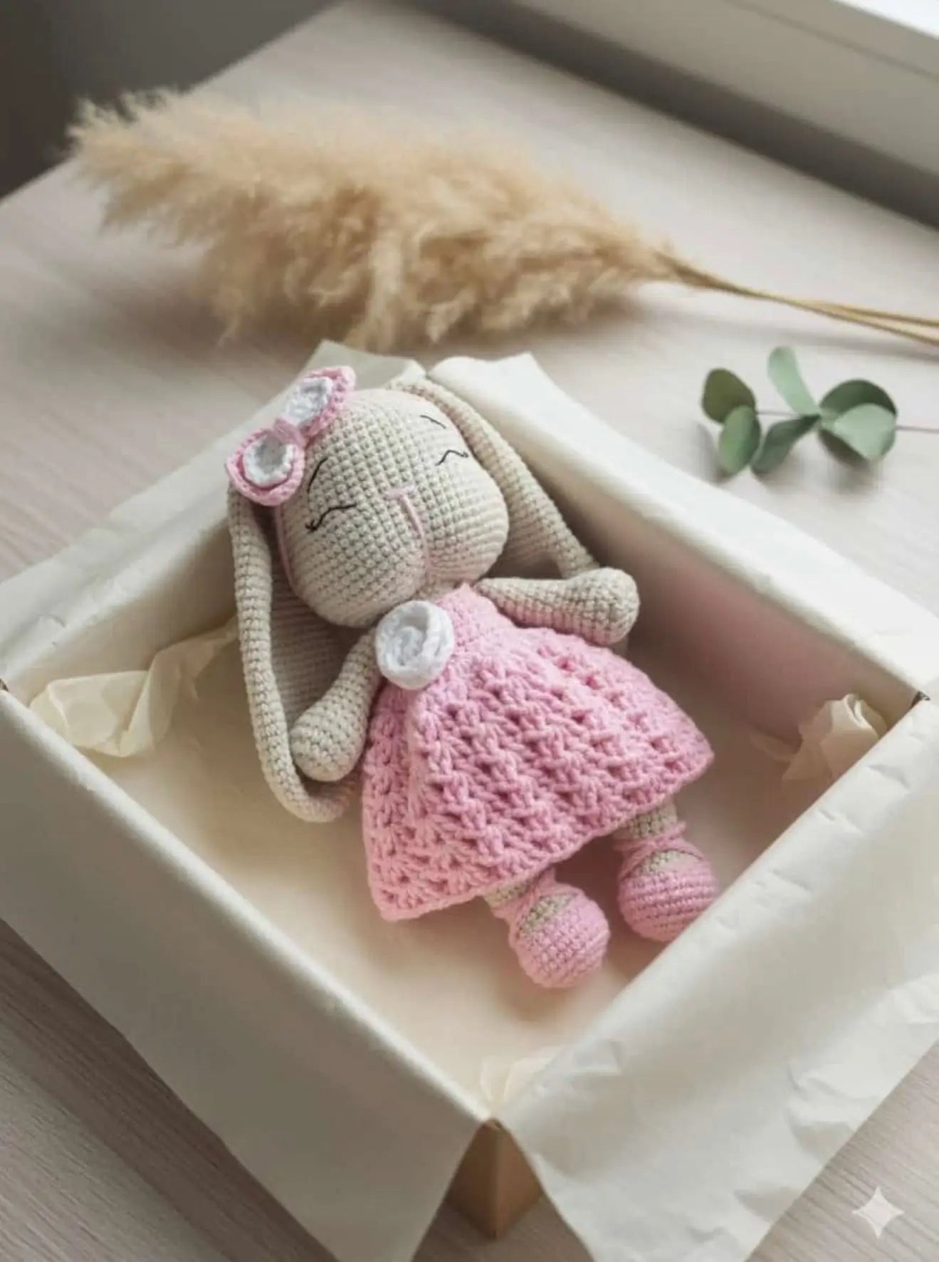 Crocheted bunny doll in pink dress with bow, nestled in a white gift box