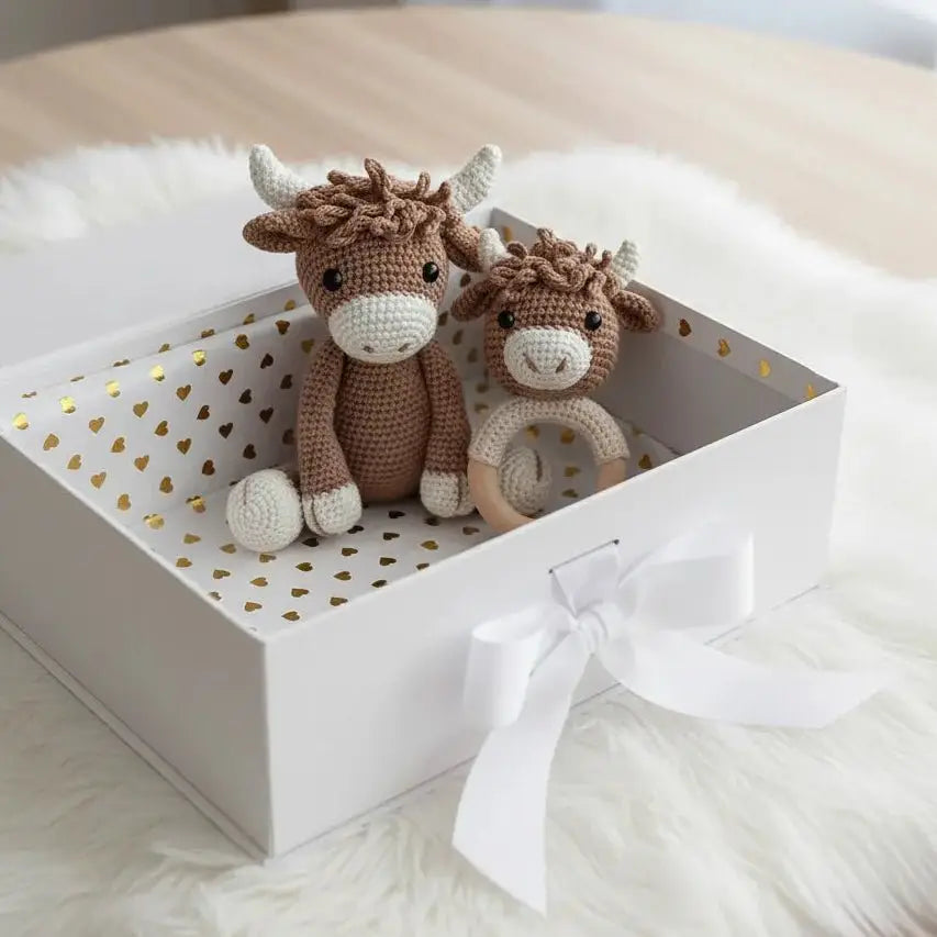 Two crocheted Highland cow stuffed animals in a white gift box with gold hearts