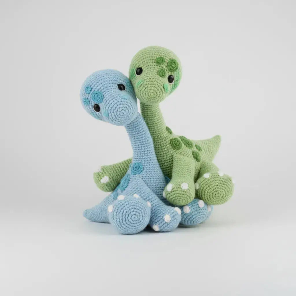 Two crocheted dinosaurs, one blue and one green, sitting close together on a white background.