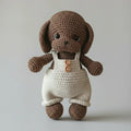 Crocheted brown puppy wearing white overalls with two wooden buttons