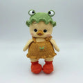 Crocheted chick doll with frog hat, yellow and orange, standing on neutral background