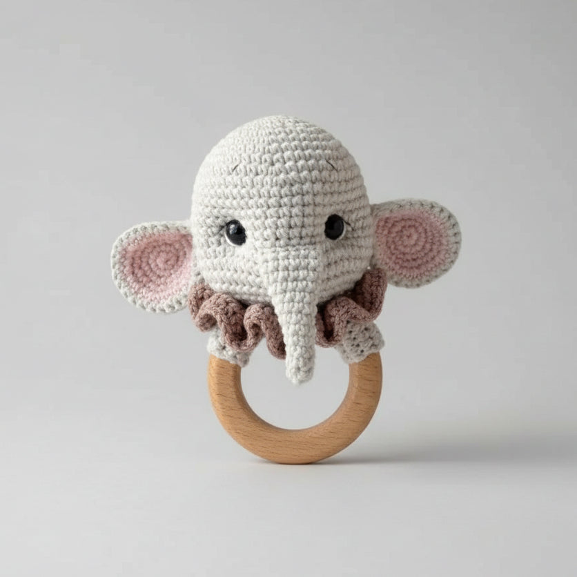 Crocheted elephant baby rattle with wooden ring, held against green blurred background