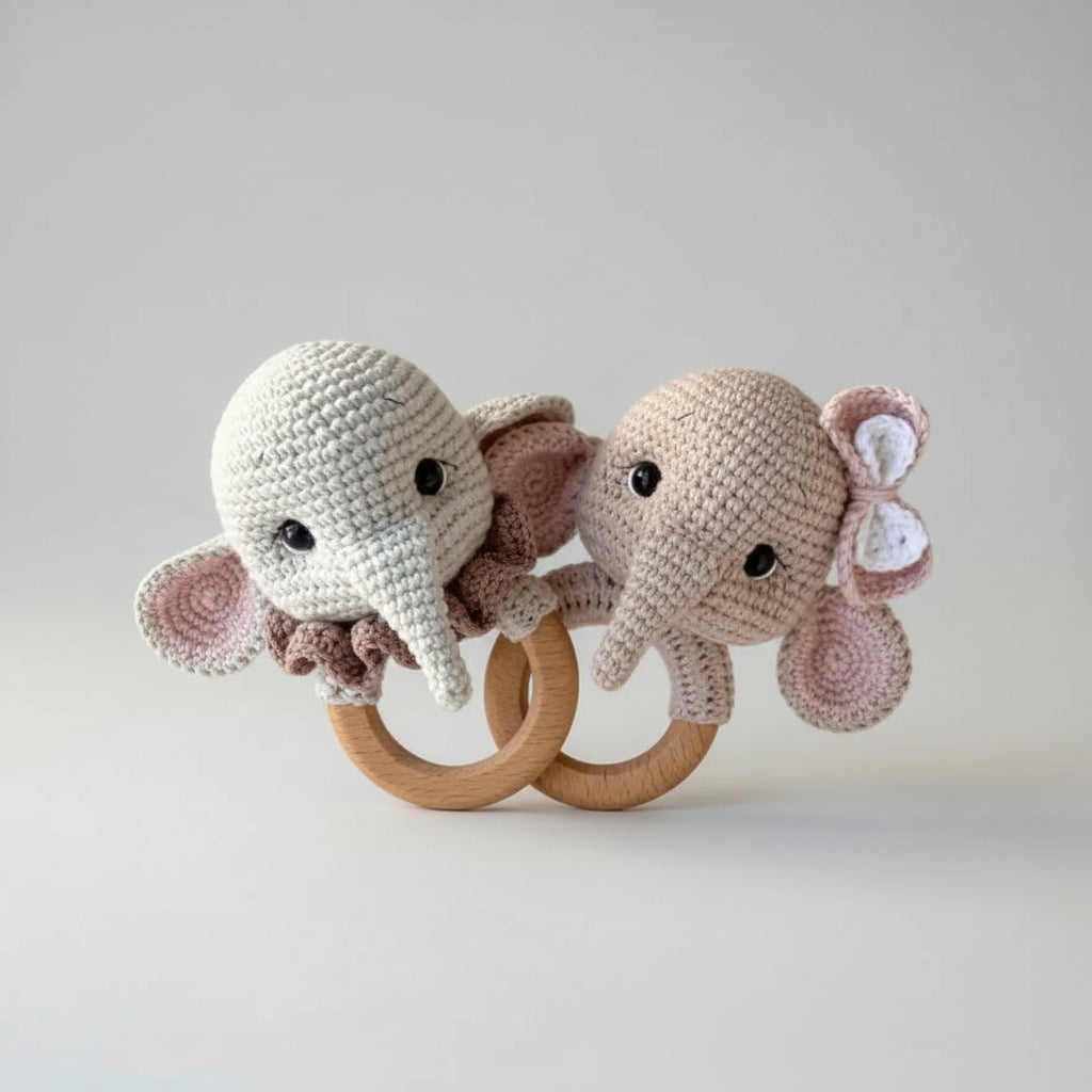 Crocheted elephant baby rattles on wooden rings, held by a hand outdoors
