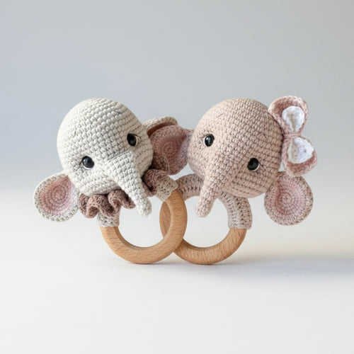 Crocheted elephant baby rattles on wooden rings, held by a hand outdoors