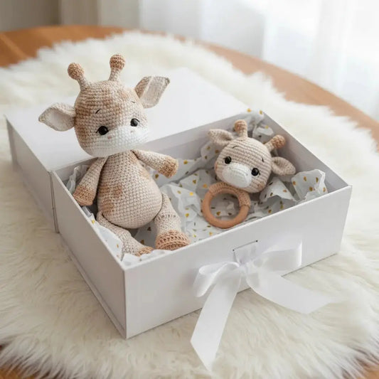 Crocheted giraffe and baby rattle in a white gift box on soft fur background