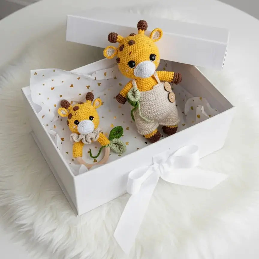 Crocheted yellow giraffe toys in a white gift box with ribbon, sitting on fluffy fabric