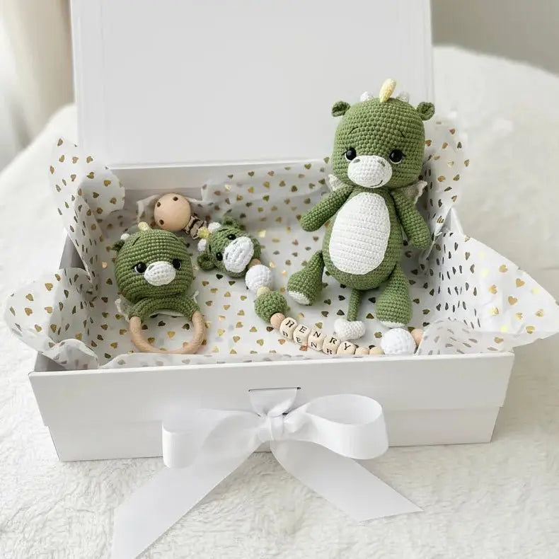 Green crocheted dragon toys and baby accessories in a white gift box with hearts