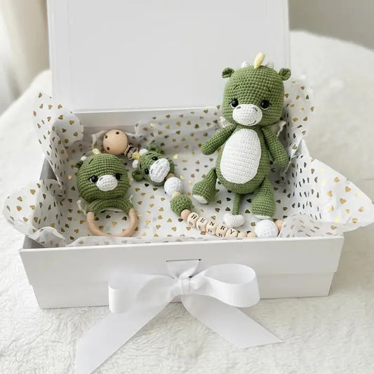Green crocheted dragon toys and baby accessories in a white gift box with hearts