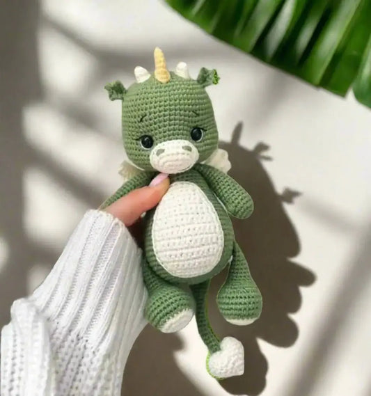 Green crocheted dragon stuffed animal with white belly, held by a knitted sleeve