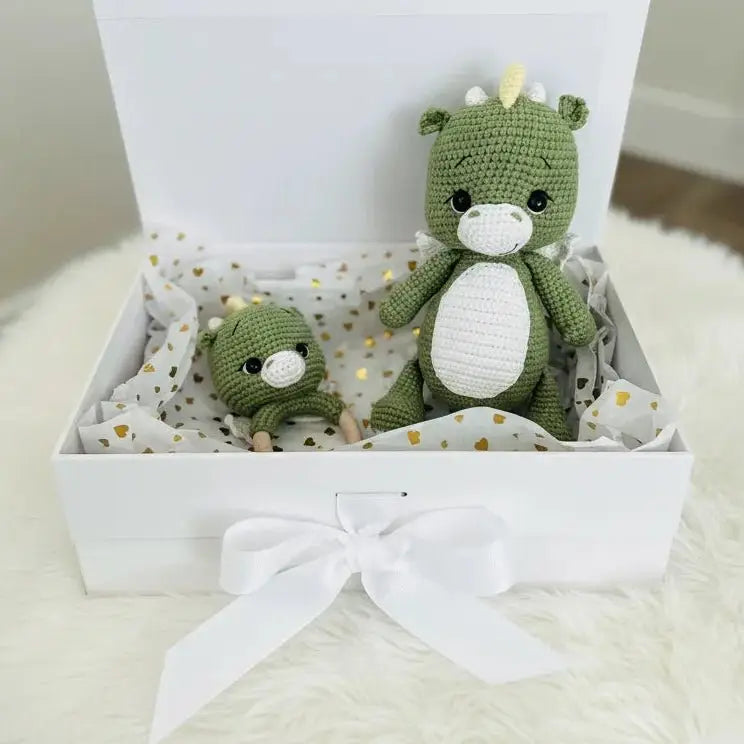 Green crocheted dinosaur stuffed animals in a white gift box with gold heart pattern