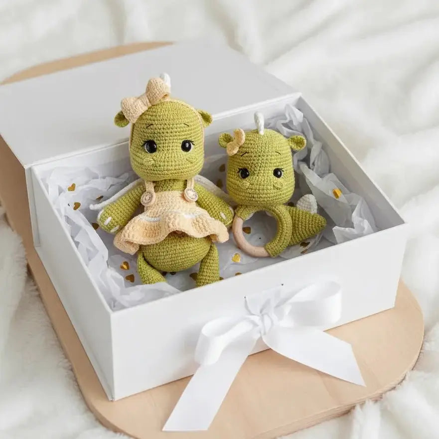 Two green crocheted dolls with bows in a white gift box with tissue paper and a white ribbon.