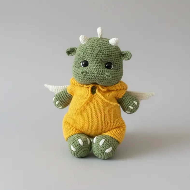 Crocheted green dragon stuffed animal wearing a yellow sweater on gray background